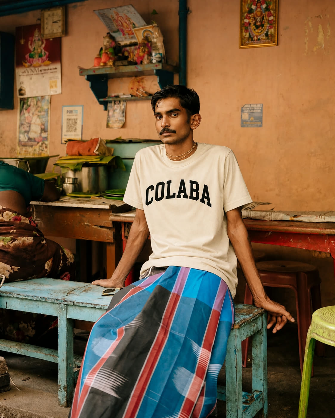 A man seated in a room wearing the Colaba tee